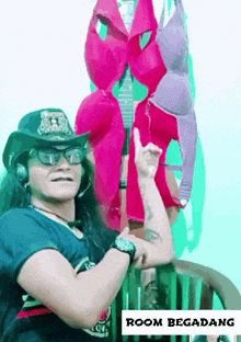 a man wearing a cowboy hat and sunglasses stands in front of a bunch of bras hanging on a wall