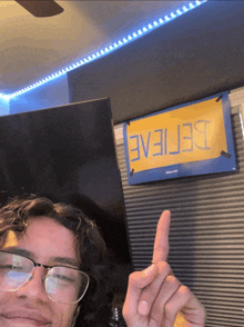 a man wearing glasses is pointing at a sign that says believe