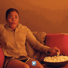 a woman sitting on a couch with a bowl of popcorn