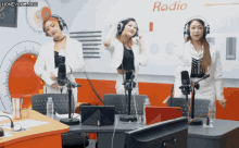 three women wearing headphones are standing in front of microphones in a radio studio