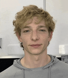 a young man with blonde hair is wearing a grey sweatshirt