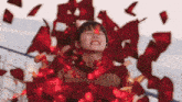 a woman is surrounded by red petals falling from the sky