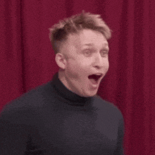 a man wearing a black turtleneck is laughing with his mouth open .