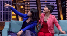 two women are sitting on a couch and one of them is pointing up at the sky