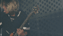 a man wearing a ska 01 shirt is playing a bass guitar