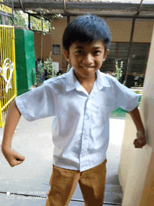 a young boy flexes his muscles while wearing a white shirt and brown pants taken by a redmi 9 ai quad camera
