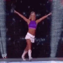 a woman in a purple top and white skirt is dancing on stage