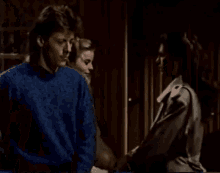 a man in a blue sweater and a woman in a trench coat are standing next to each other .