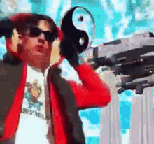 a man wearing sunglasses and a red jacket is holding a gun and a yin yang symbol