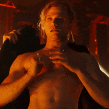a shirtless man with long blonde hair is holding a black jacket over his shoulder