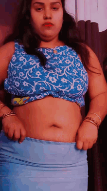 a woman wearing a blue top and blue skirt shows off her belly