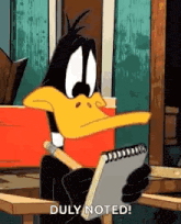 daffy duck is sitting at a table holding a notebook and a pen .