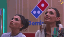 two women are sitting in front of a domino 's pizza sign .