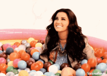 a woman is sitting in a pool of balls with edits portirroni written on the bottom