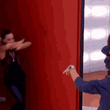 two women are standing next to each other in front of a red wall . one of the women is wearing a watch .