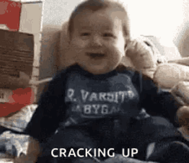a baby is sitting on a couch wearing a shirt that says varsity on it .