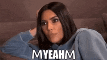 a woman is sitting on a couch with her hand on her head and the words `` myeahm '' written on her face .