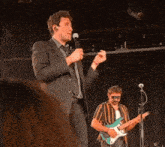 a man singing into a microphone while another man plays guitar