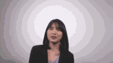 the woman is wearing a black jacket and a purple shirt and is making a funny face .