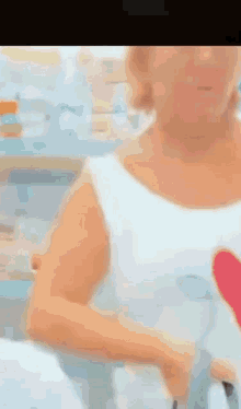 a woman in a white tank top with a red heart on it is standing in a kitchen .