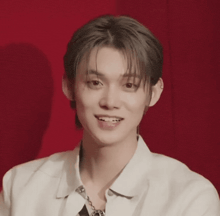 a young man wearing a white shirt and a chain around his neck is smiling .