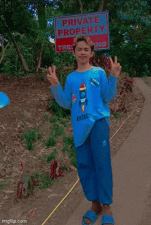 a boy wearing a blue shirt with a rocket on it stands in front of a sign that says private property