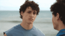 a man with curly hair looks at another man on the beach