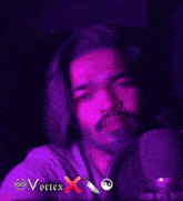 a man with long hair and a beard looks at the camera with purple lights behind him and the word vortex on the bottom right