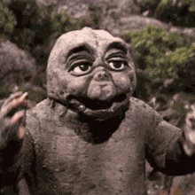 a statue of a dinosaur is standing in the woods with its arms outstretched and smiling .