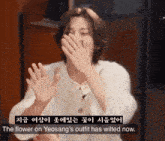 a woman covering her mouth with her hands and the words " the flower on yeosang 's outfit has wilted now " next to her