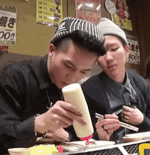 a man is pouring mayonnaise on a plate while another man looks on