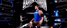 a wrestler in a blue shirt is holding a championship belt in front of a sign that says the next big thing