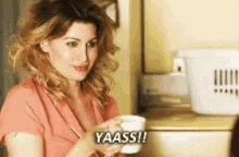 a woman in a pink shirt is holding a cup of coffee and saying yaass .