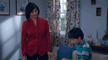 a woman in a red sweater is standing next to a boy in a living room .