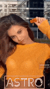 a woman in a yellow sweater is holding a flower in front of a building .