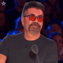 a man wearing red glasses and a black shirt is smiling in front of a microphone