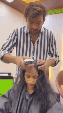 a man in a striped shirt is cutting a woman 's hair in a hair salon .