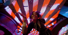 a woman with purple hair is dancing in front of a colorful light display