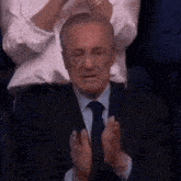a man in a suit and tie is clapping his hands while sitting in a crowd .