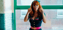 a woman with red hair is standing in front of a window wearing a pink belt that says ' sss ' on it