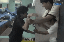 two men are standing next to each other in a room . one of the men is holding the other 's hand .