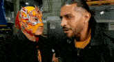 a man wearing a mask talks to another man wearing a black jacket
