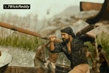 a man with a beard is holding a wooden pole in front of a 7wickreddy logo