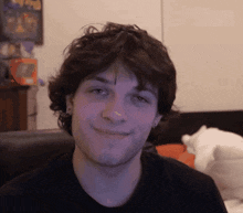 a young man with curly hair is smiling and looking at the camera
