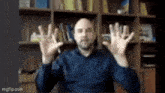 a man in a blue shirt is sitting at a desk with his hands up in the air .