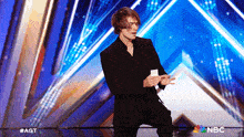 a man in a suit stands on a stage with a nbc logo in the corner