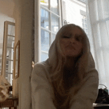 a woman is wearing a white hoodie and sitting in front of a window .