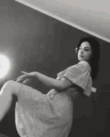 a black and white photo of a woman in a plaid dress sitting on the floor .
