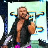 a man in a leather jacket is standing in front of a large screen with the letter t.