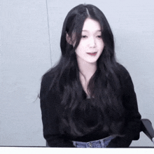 a woman with long black hair is wearing a black sweater and jeans